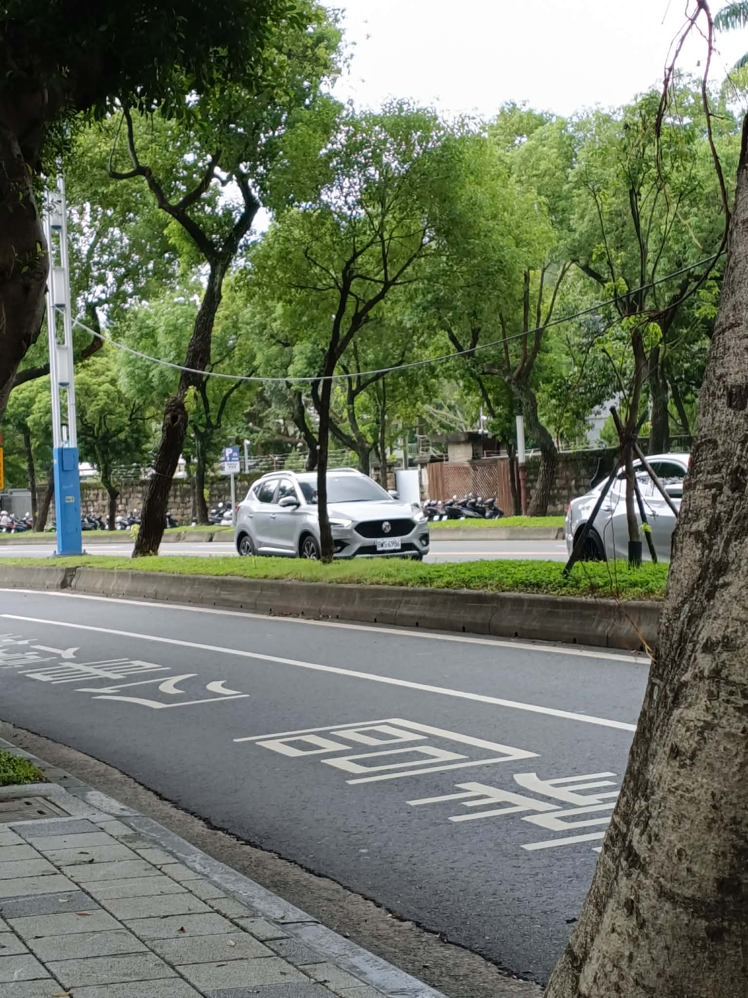 A wide road near Ming Chuan University with clear lane markings, parked motorbikes off to the side, and trees lining the street