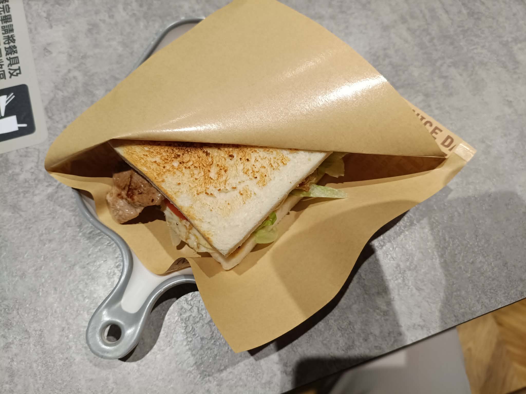 A toasted sandwich with meat, lettuce, and tomato, wrapped in brown paper from a brunch shop on Wuhua Road